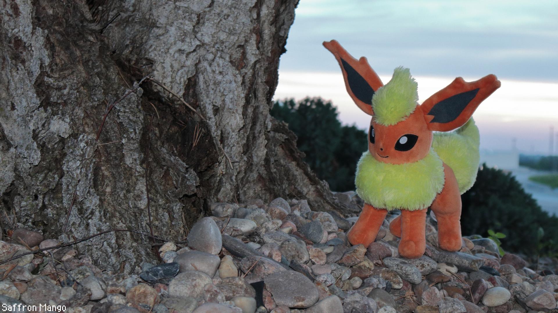A flareon next to a tree on top of some rocks, trees fill the background.