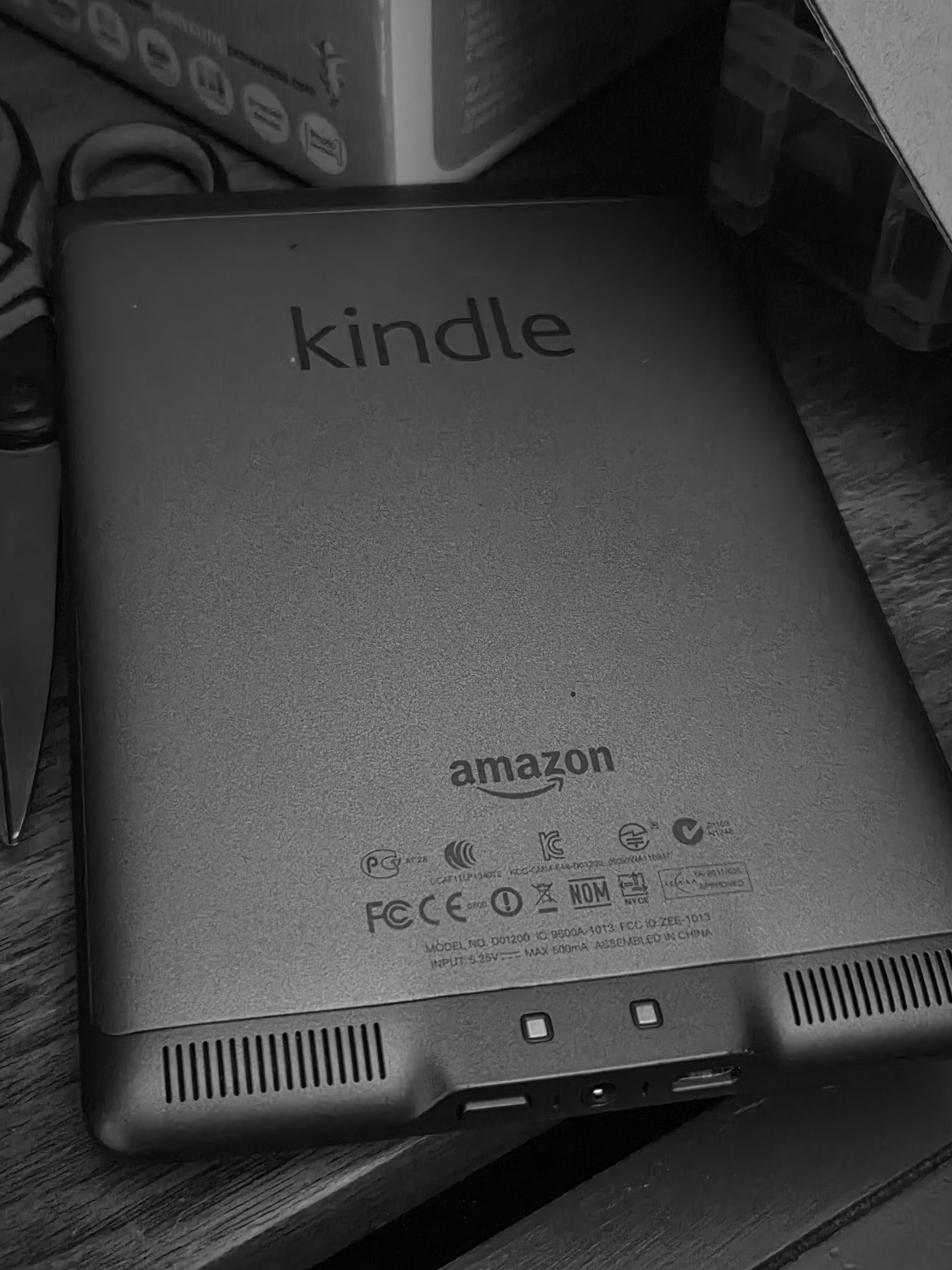 Black and White image of the backside of a Kindle Touch on a dresser.